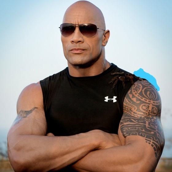 Foto de (Dwayne “The Rock” Johnson) posant amb els braços creuats, amb ulleres de sol i una samarreta de tirants.